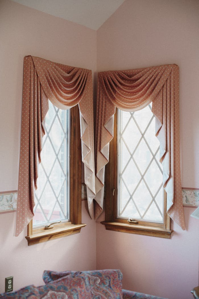 Elegant draped curtains complement a modern interior with soft pink walls and wooden frames for a cozy home feel.